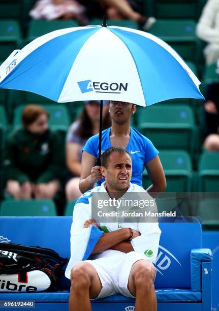 Marius Copil of Romania shelters under an umbrella as rain delay play during his Men's second round match against Reilly Opelka of the USA during day...