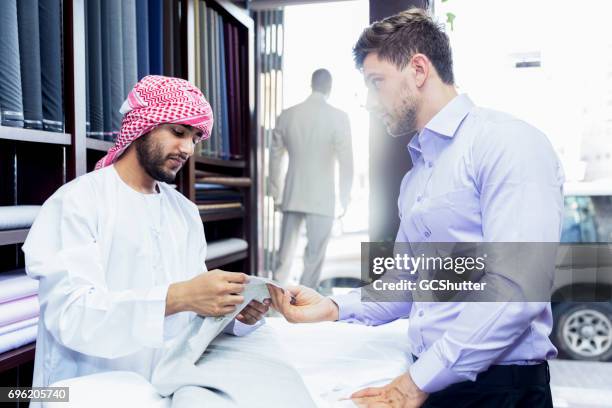 middle eastern man demonstrating the quality of his product to a customer - dubai shopping stock pictures, royalty-free photos & images