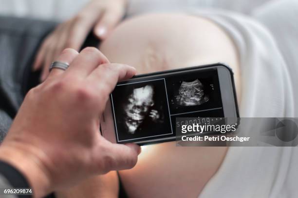 a young couple using a mobile device to look at their unborn baby. - sonhar stock pictures, royalty-free photos & images