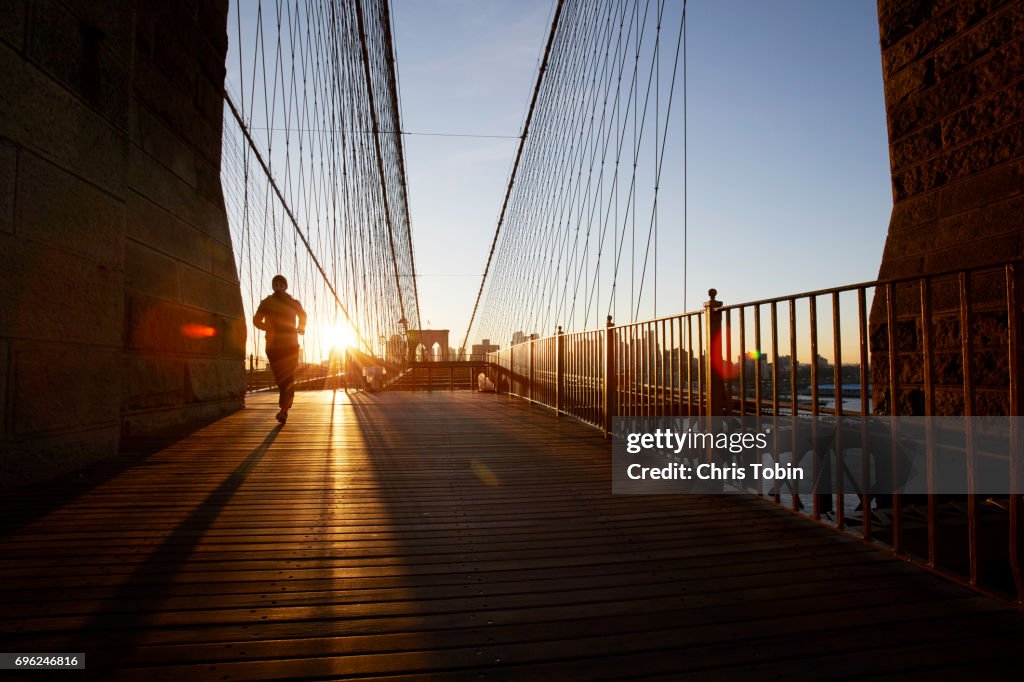 Silhouette of jogger on Brooklyn Bridge at sunset