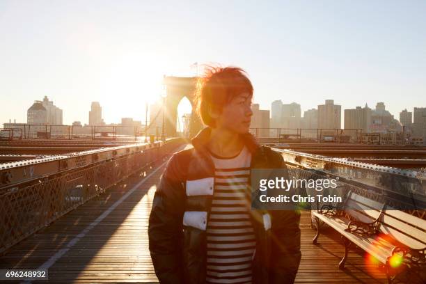sun and lens flare in background of young man standing on brooklyn bridge - new york personas stock-fotos und bilder