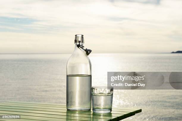 series of images with a bottle and glass of water with setting sun and sea in background - bottiglia vetro foto e immagini stock