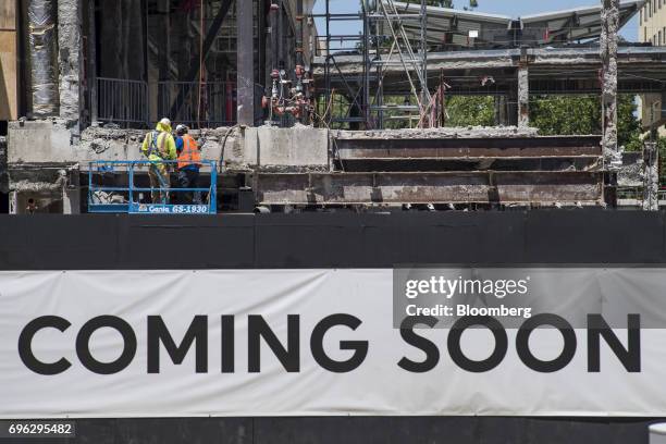 Workers stand on a cherry picker above a "Coming Soon" sign displayed at a building under construction in Sacramento, California, U.S., on Tuesday,...