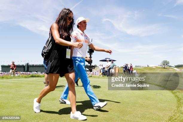 Rickie Fowler of the United States walks from the ninth green with Allison Stokke after finishing during the first round of the 2017 U.S. Open at...