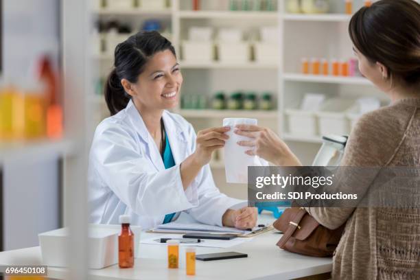 smiling female pharmacist hands medication to customer - prescription stock pictures, royalty-free photos & images