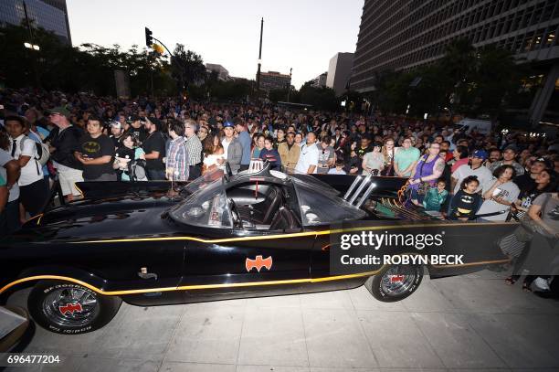 Fans gather around a Batmobile before a tribute to "Batman" star Adam West that includes lighting a Bat-signal at City Hall, June 15 in Los Angeles,...