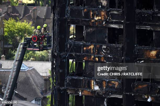 Firemen, perched on an extendable ladder raise, inspect the remains of Grenfell Tower, a residential tower block in west London which was gutted by...