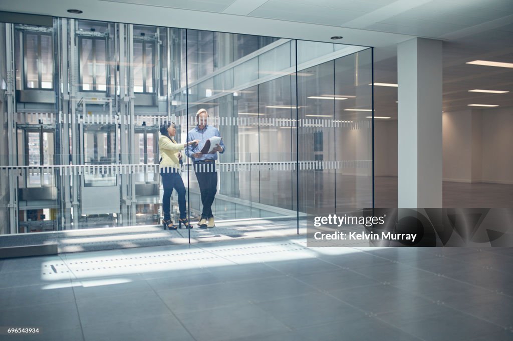 Work colleagues discussing project in office hallway