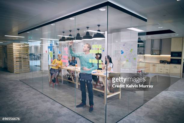 work colleagues brainstorming in creative office - glaswand stock-fotos und bilder