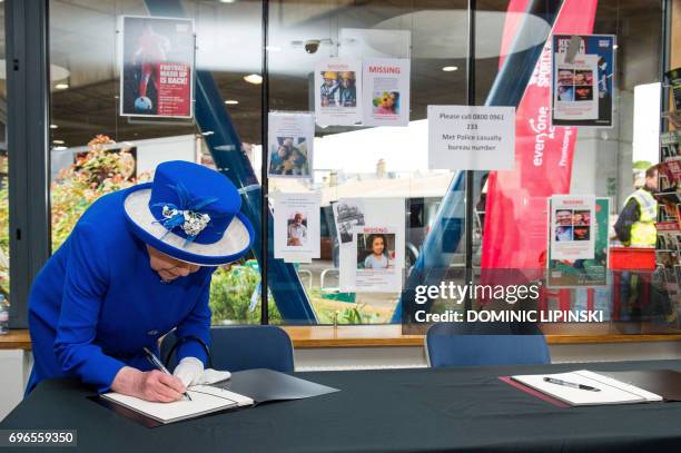 Britain's Queen Elizabeth II signs a book of condolences during a visit to the Westway Sports Centre which is providing temporary shelter for those...
