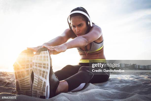 fit woman stretching on the beach before working out - girl with earphones stock pictures, royalty-free photos & images