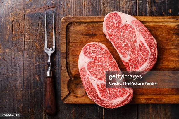 raw fresh marbled meat steak ribeye black angus and meat fork on wooden background copy space - carne de vaca wagyu fotografías e imágenes de stock