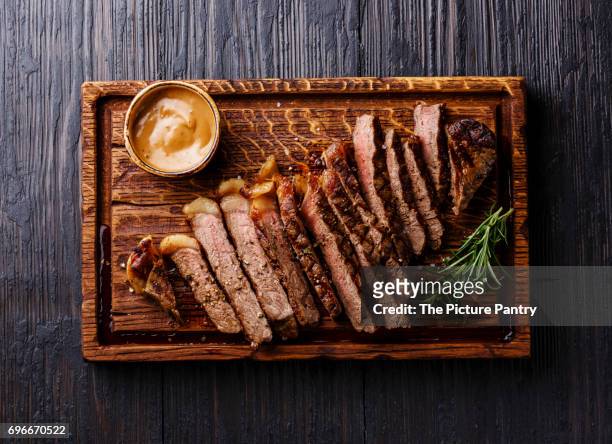 sliced grilled well done striploin steak with pepper sauce on cutting board on burned black wooden background - lob wedge stock-fotos und bilder
