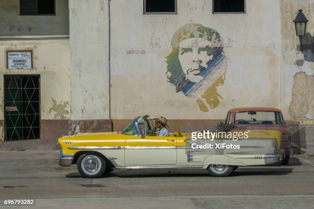 vintage car passes by che guevara icon on wall in havana - che guevara stock pictures, royalty-free photos & images