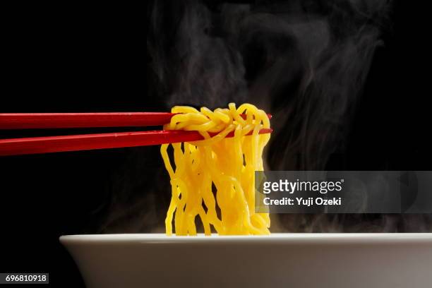 sapporo ramen noodle lifted up by red chopsticks with steam against black background - ramen noodles stock pictures, royalty-free photos & images