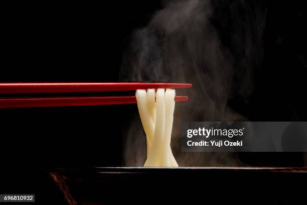 japanese udon noodle lifted up by red chopsticks with steam against black background - udon noodle stock pictures, royalty-free photos & images