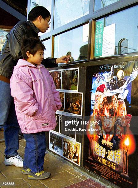 Young girl looks at a Harry Potter movie poster, while her father purchases tickets, in front of the box office of a movie theatre during the movies...