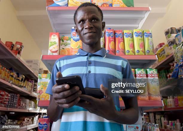 Senegalese grocer and Weebi user Amadou Bousso poses with smartphones at his shop in Dakar, on March 23, 2017. Corner shops, markets and street...