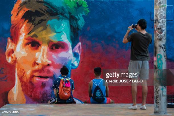 Two joung men look at a graffiti portraying Barcelona's Argentinian forward Lionel Messi as another one takes photos on June 17, 2017 in Barcelona. /...