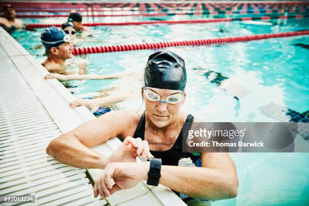 mature female swimmer checking fitness watch during morning workout in outdoor pool - fitnesstracker stock pictures, royalty-free photos & images
