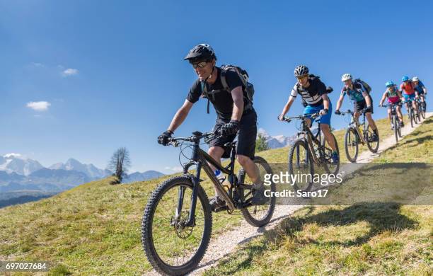 large group of mountainbikers downhill in front of mt. marmolada, italy - mountainbiker stock pictures, royalty-free photos & images