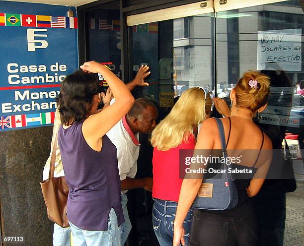 Customers try to enter a currency exchange house February 13, 2002 in Caracas, Venezuela. The notice fixed on the glass door reads "Dollars in cash,...