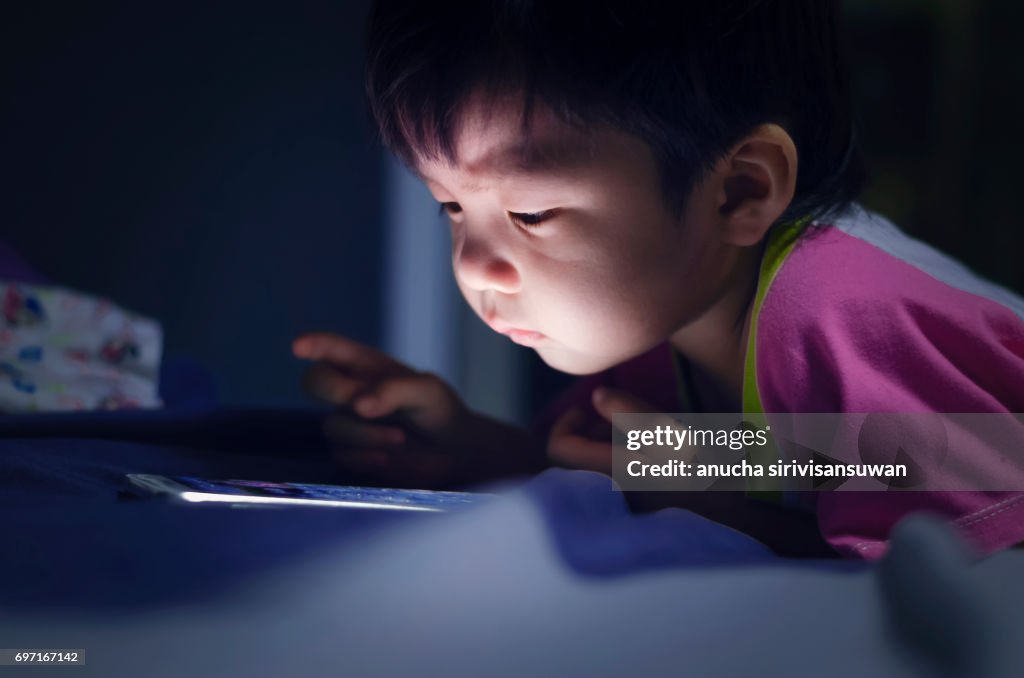 Kid with tablet in the dark on bed and reading at Night .