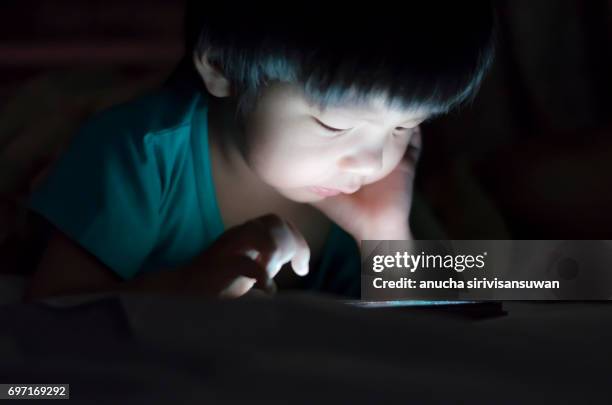 kid with tablet in the dark on bed and reading at night . - nursery night stock pictures, royalty-free photos & images