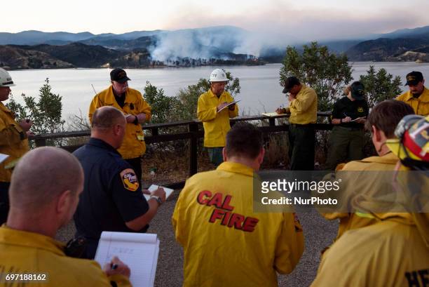 Firefighters during an evening briefing as the Castaic Lake fire burns in the background. Castaic, California on June 17, 2017. Firefighters battle...