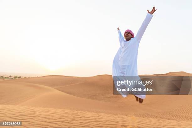 cheerful young arab man jumping on the sand dunes - bahrain tourism stock pictures, royalty-free photos & images