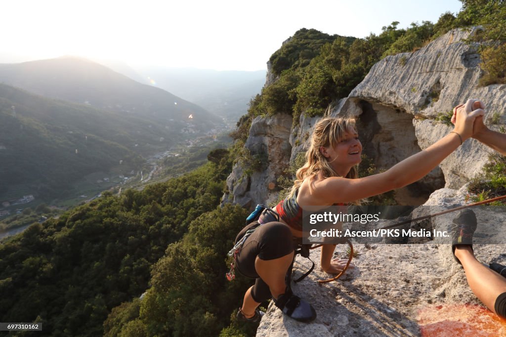 Young female climber ascends vertical rock, to belayer