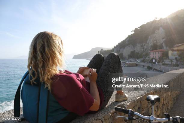 woman relaxes above sea with bike, writes in journal - jeggings stock pictures, royalty-free photos & images