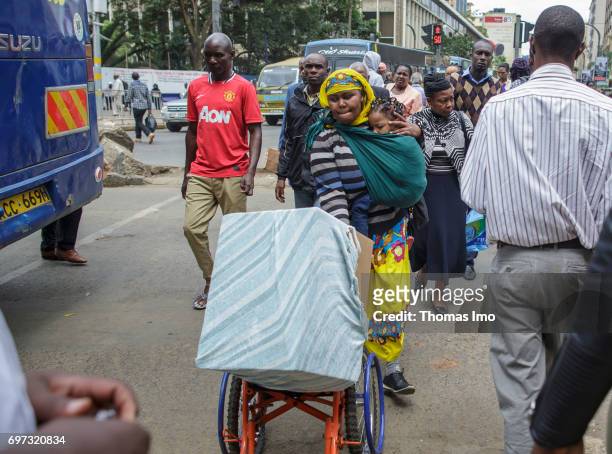 Nairobi, Kenya A mother carries her daughter in a baby sling while transporting a box on a wheelchair. Street scene in Nairobi, capital of Kenya on...