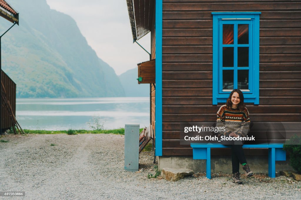 Frau sitzt auf der Bank in der Nähe das Holzhaus in Norwegen