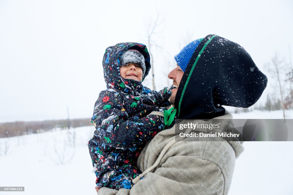 Kid covered with snow laughing with his father.