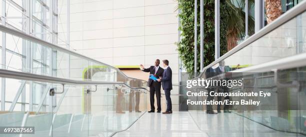 businessmen discussing plans in modern lobby - railings stock pictures, royalty-free photos & images