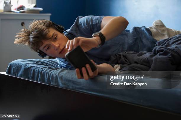 boy aged 16 on bed with headphones and smart phone - boys bedroom stock-fotos und bilder