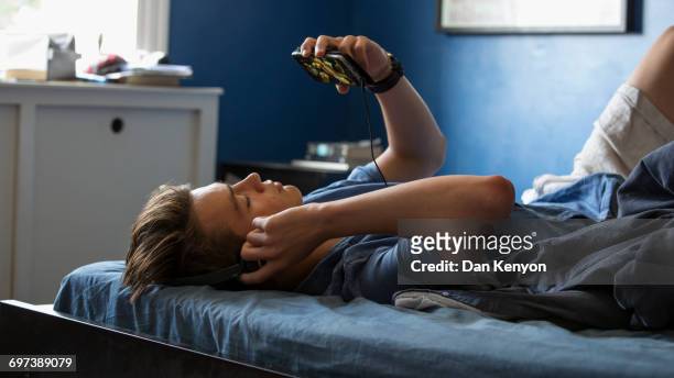 BOY AGED 16 ON BED WITH HEADPHONES AND SMART PHONE