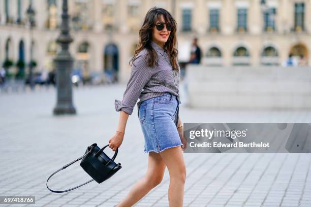 Sarah Benziane, fashion blogger, wears a The Kooples gingham shirt, a New Look blue denim skirt, an Ali Express bag, sunglasses, and Zara white...