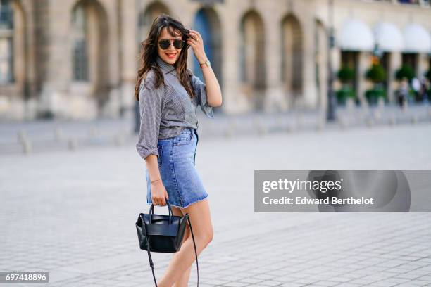 Sarah Benziane, fashion blogger, wears a The Kooples gingham shirt, a New Look blue denim skirt, an Ali Express bag, sunglasses, and Zara white...