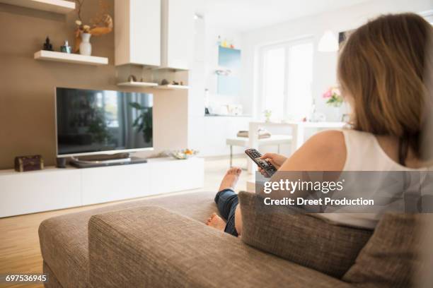 pregnant woman sitting on sofa and watching tv with remote control, munich, bavaria, germany - back cushion stock pictures, royalty-free photos & images