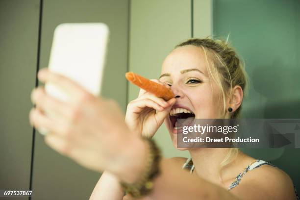 young woman taking a selfie and making snowman with a carrot on her face, munich, bavaria, germany - frau schneemann stock-fotos und bilder