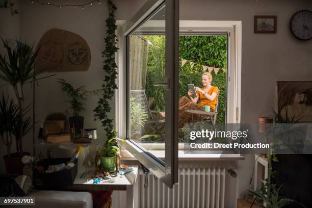 beautiful young woman using digital tablet and having cup of tea in the domestic garden, munich, bavaria, germany - bavarian man in front of house stock-fotos und bilder