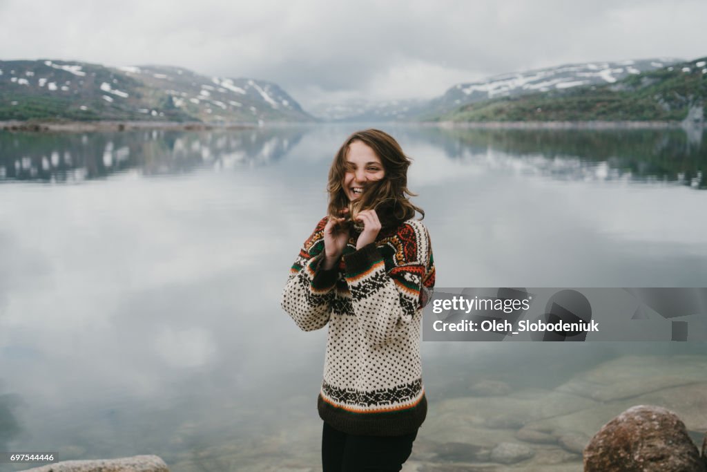 Mujer en punto jersey riendo junto al fiordo en Noruega