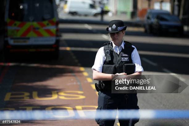 Police officer observes a minutes' silence in memory of the victims of the June 14 Grenfell Tower fire, as she stands on duty by a police cordon in...