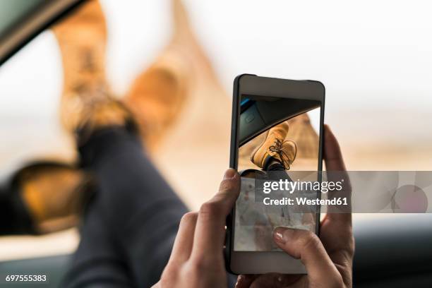 spain, navarra, bardenas reales, young woman with legs of leaning out of car window taking selfie - mobile phone in hand driving stock pictures, royalty-free photos & images