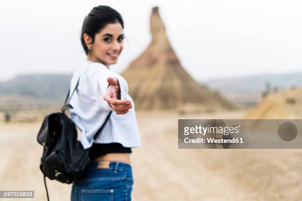 spain, navarra, bardenas reales, smiling young woman reaching out her hand to viewer - veleiding stockfoto's en -beelden