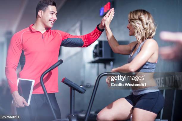 fitness instrustor high fiving with woman on exercise machine - happy caucasian woman on elliptical trainer at gym stock pictures, royalty-free photos & images