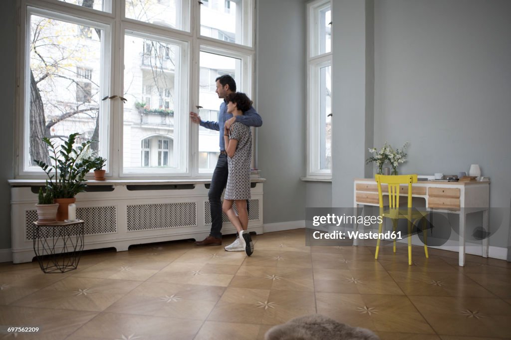 Couple looking together through window at home
