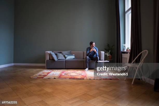 man sitting on couch at home looking through window - sofa stock-fotos und bilder